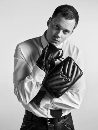 Bill Skarsgard holding a black leather Saint Laurent handbag in a monochrome fashion campaign portrait