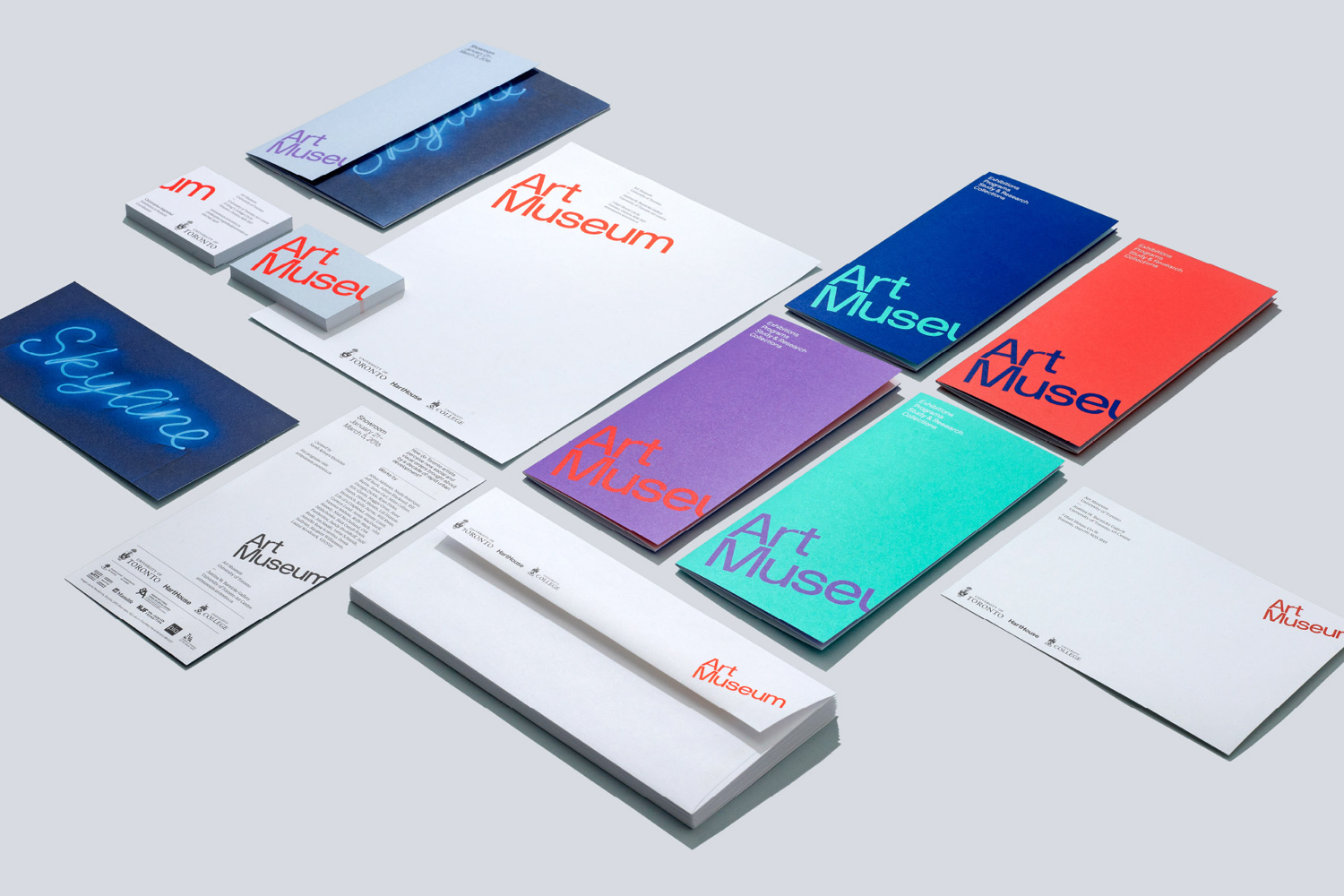Flat lay of brand identity stationery including envelopes, business cards, and brochures with colorful typography on light background.