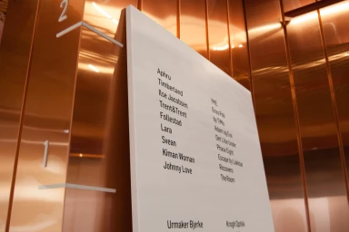 White directory sign mounted on polished copper elevator wall with brand names
