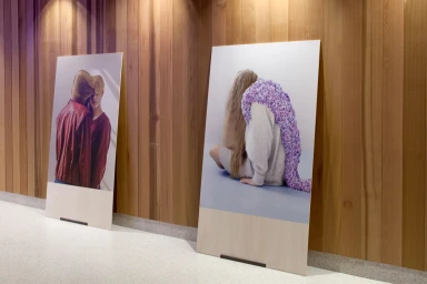 Two large vertical posters featuring fashion photography displayed against a vertical wooden slat wall on a terrazzo floor.