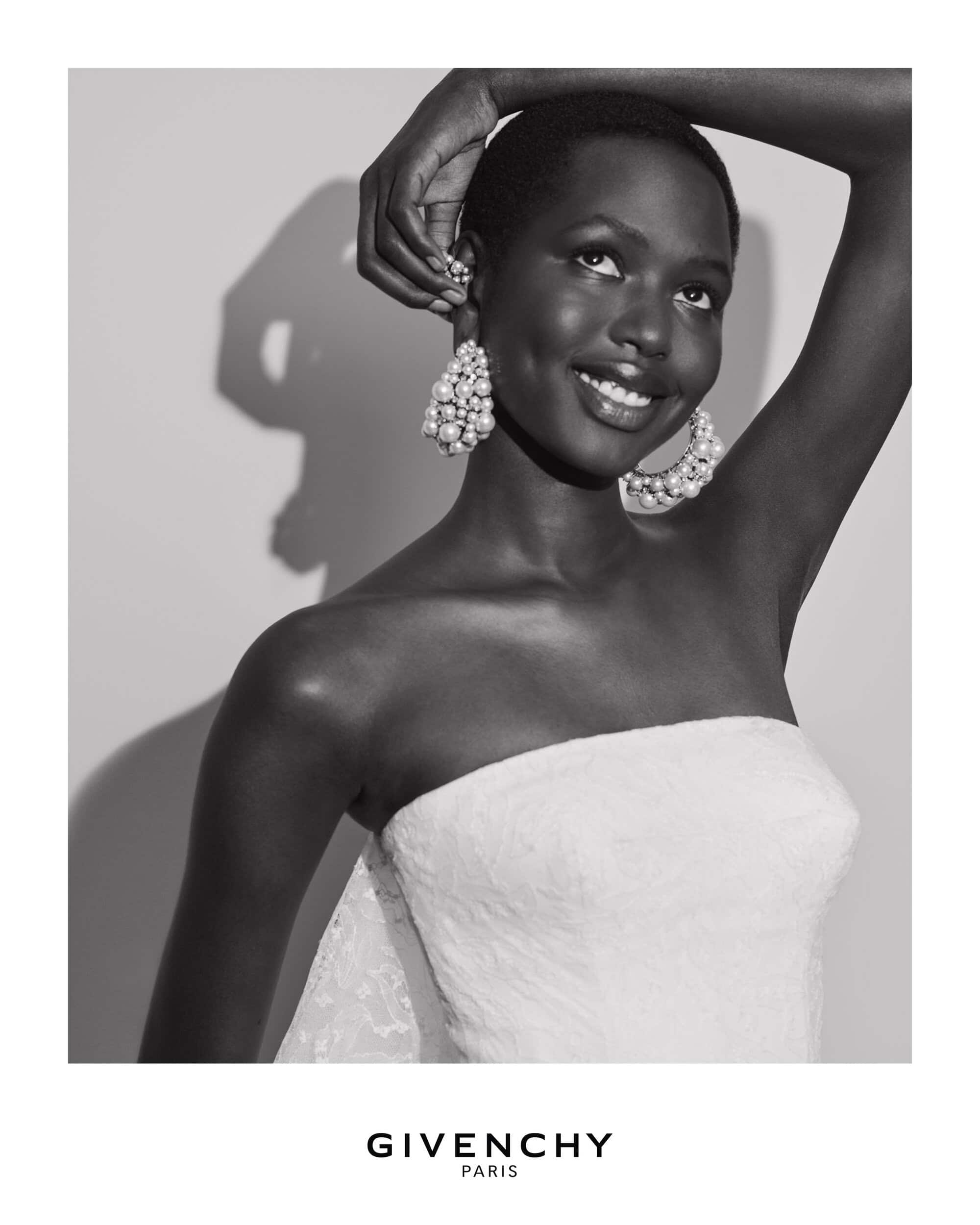 Black and white portrait of a smiling Black model wearing pearl cluster earrings and a strapless white top.
