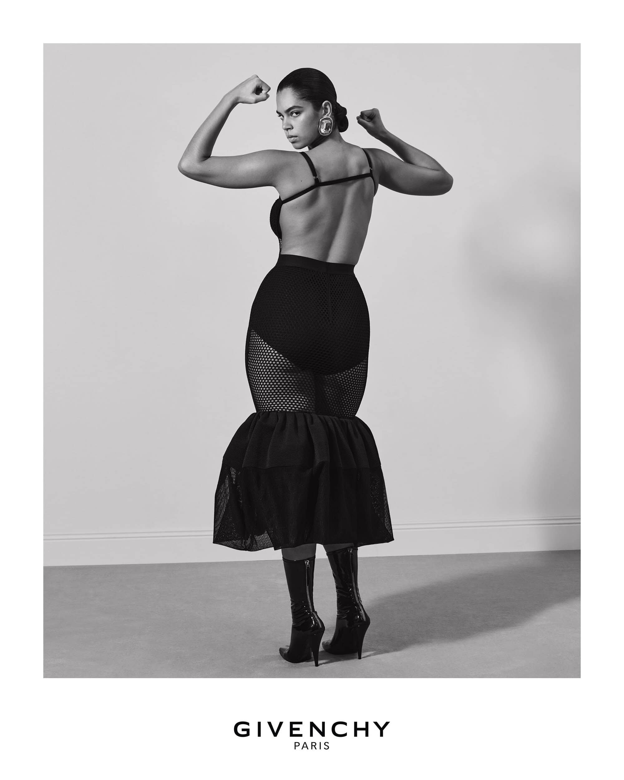 Model in black dress flexing biceps in Givenchy Fall 2025 campaign shot by Collier Schorr against a plain grey studio backdrop
