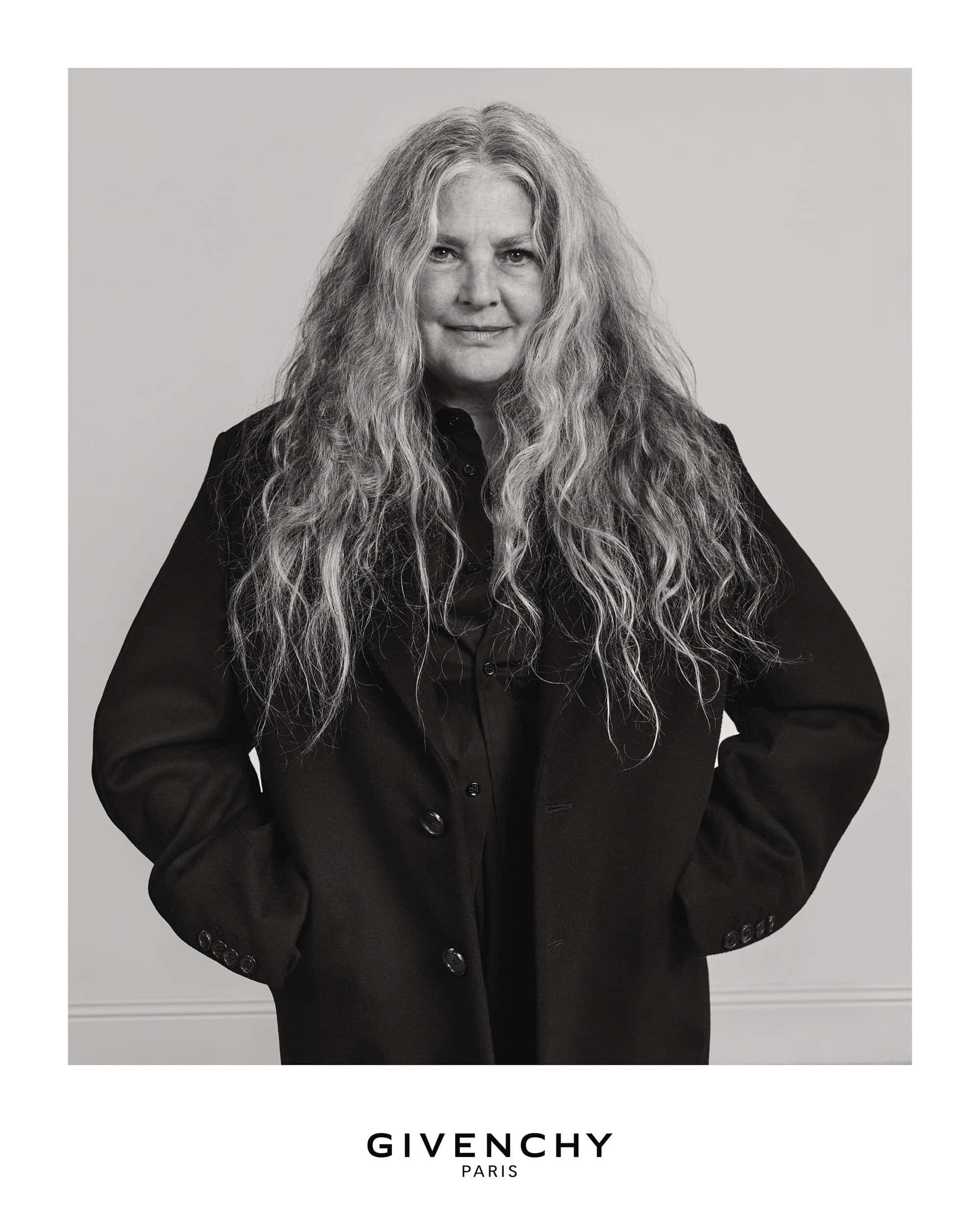 Portrait of an older woman with long grey hair wearing a dark coat against a plain background for Givenchy Fall 2025.