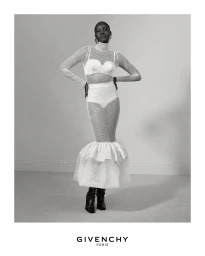 Model in white mesh turtleneck dress standing against a plain grey studio backdrop with Givenchy Paris logo below.