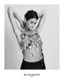 Model Kaia Gerber wearing an elaborate crystal-embellished halter top and dark trousers against a white backdrop for Givenchy.