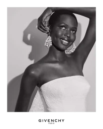Black and white portrait of a smiling Black model wearing pearl cluster earrings and a strapless white top.