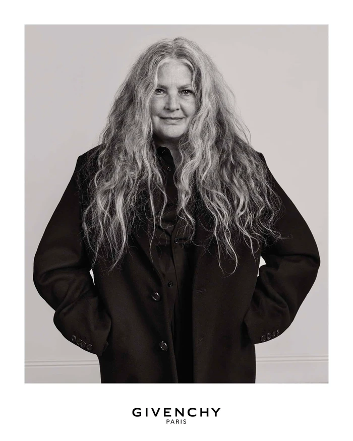 Portrait of an older woman with long grey hair wearing a dark coat against a plain background for Givenchy Fall 2025.