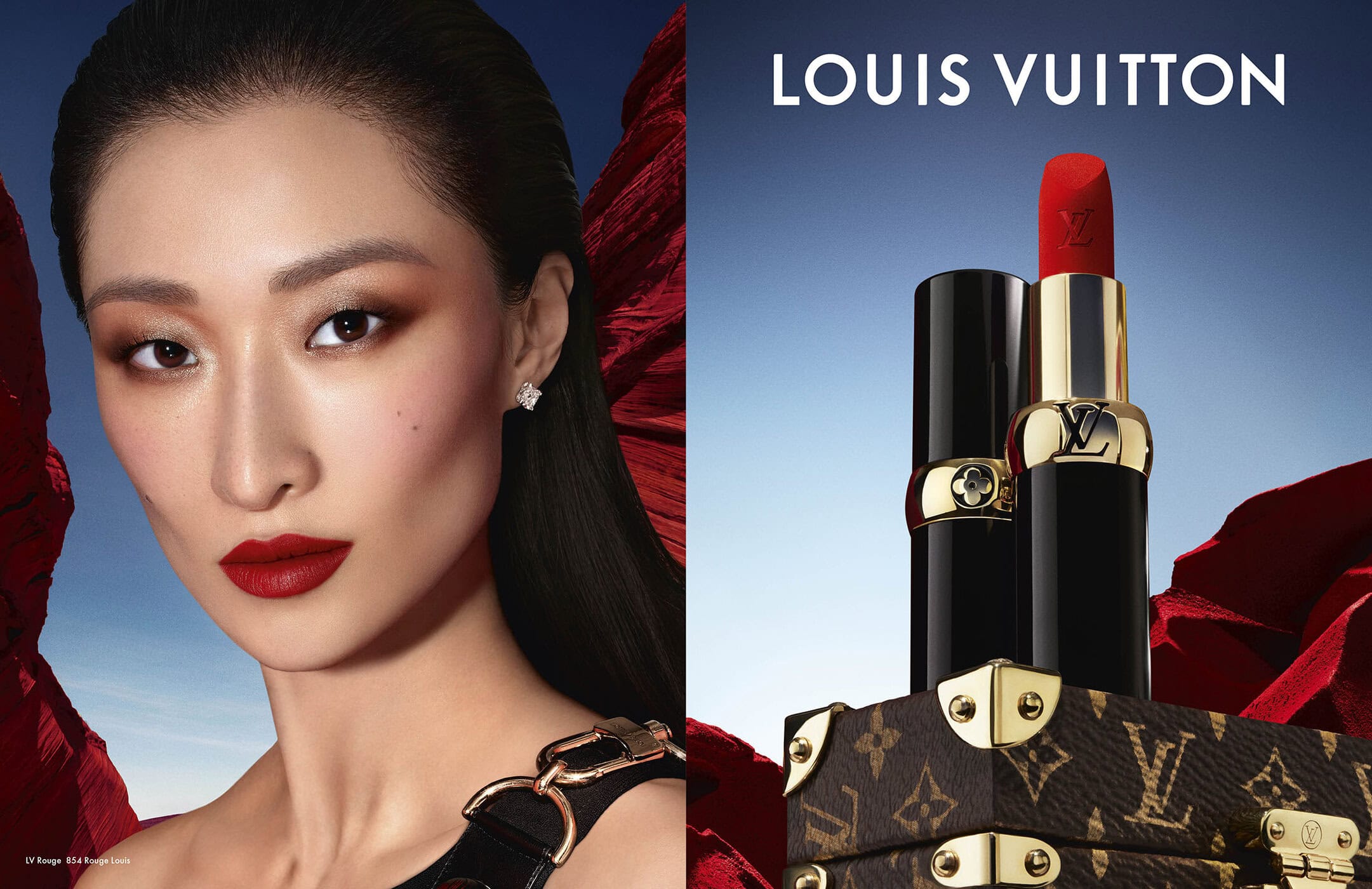 Close-up of a model wearing red lipstick beside a Louis Vuitton lipstick tube resting on a monogram trunk against a blue sky