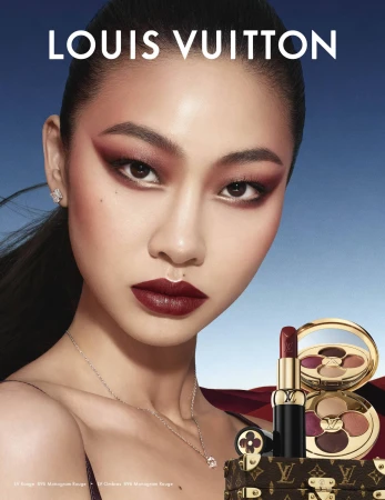 Close-up beauty portrait of a model with dramatic burgundy eye makeup and dark lipstick against a gradient blue sky.