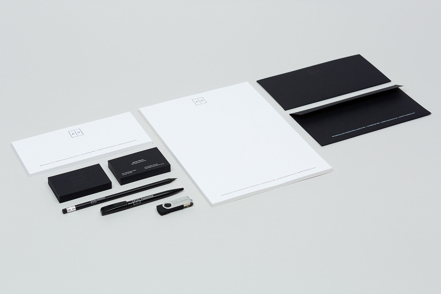 Minimalist corporate stationery set including black and white business cards, letterhead, envelopes, pens, and a USB drive on a light grey background