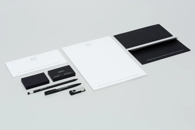 Minimalist corporate stationery set including black and white business cards, letterhead, envelopes, pens, and a USB drive on a light grey background