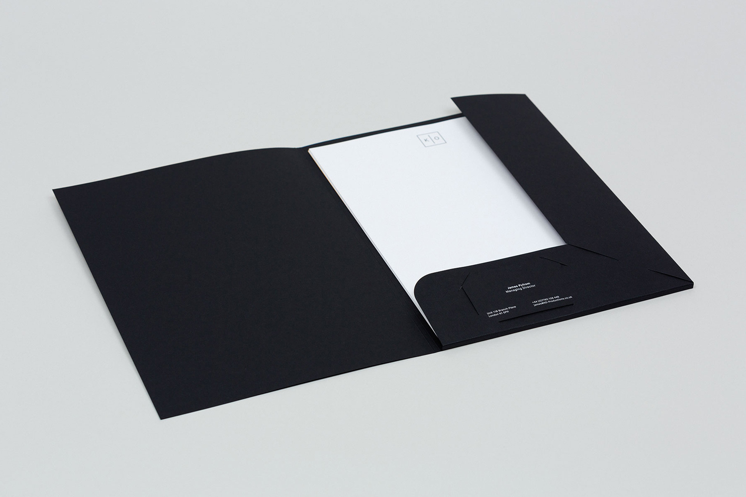 Open black folder containing white stationery and business card on a neutral grey background