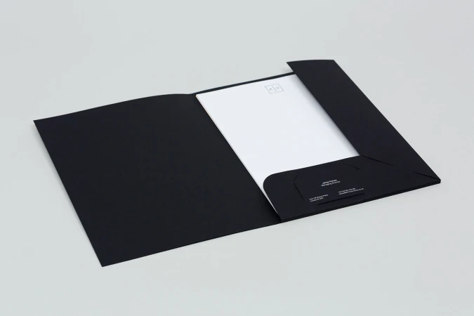 Open black folder containing white stationery and business card on a neutral grey background