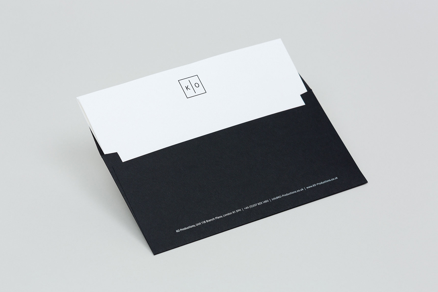 Black envelope with white insert showing minimalist KO Productions logo against a neutral light grey background