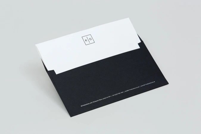 Black envelope with white insert showing minimalist KO Productions logo against a neutral light grey background