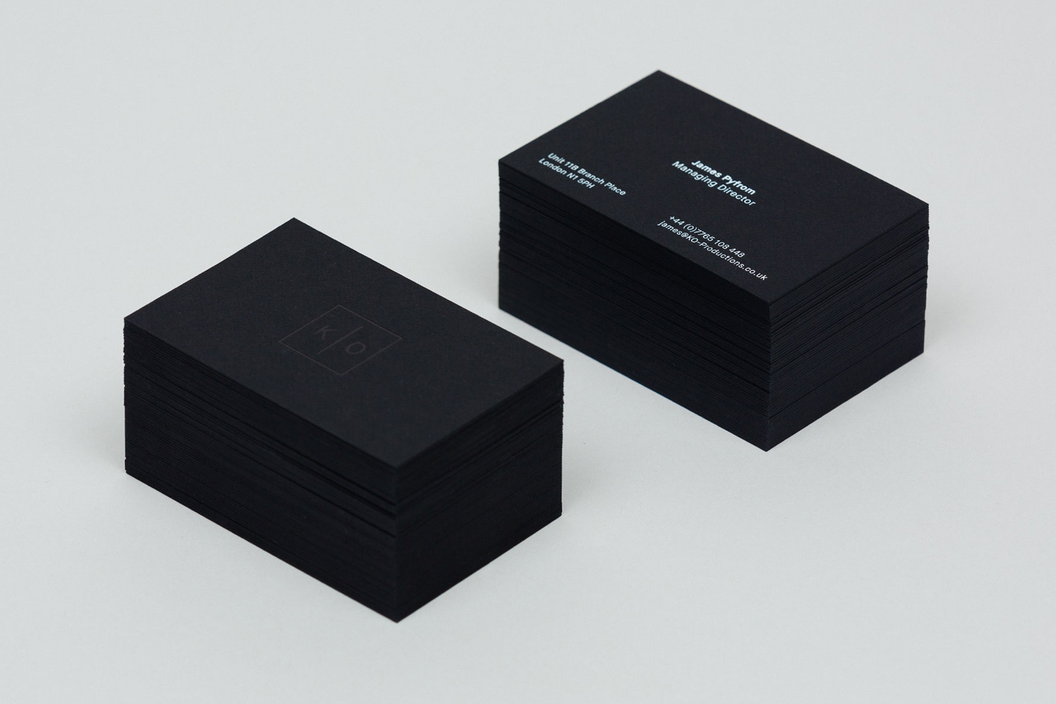 Two stacks of matte black business cards featuring white typography and a minimalist logo against a white background.