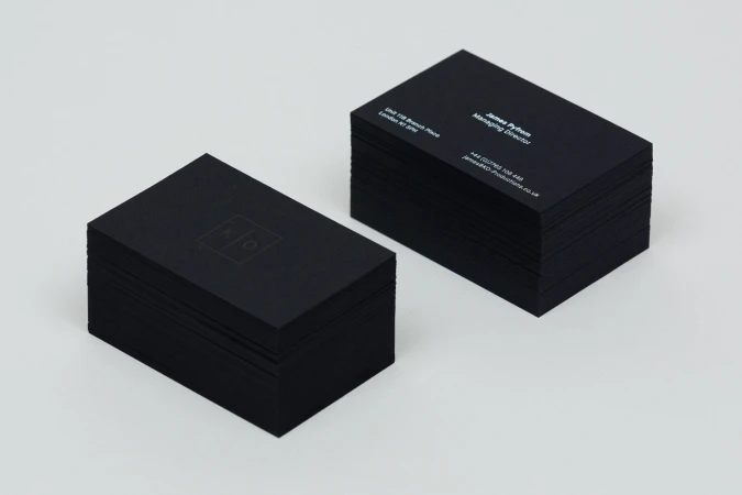 Two stacks of matte black business cards featuring white typography and a minimalist logo against a white background.