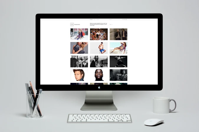 Desktop computer displaying a creative portfolio website with a keyboard, mouse, coffee mug, and a cup of pens on a white desk
