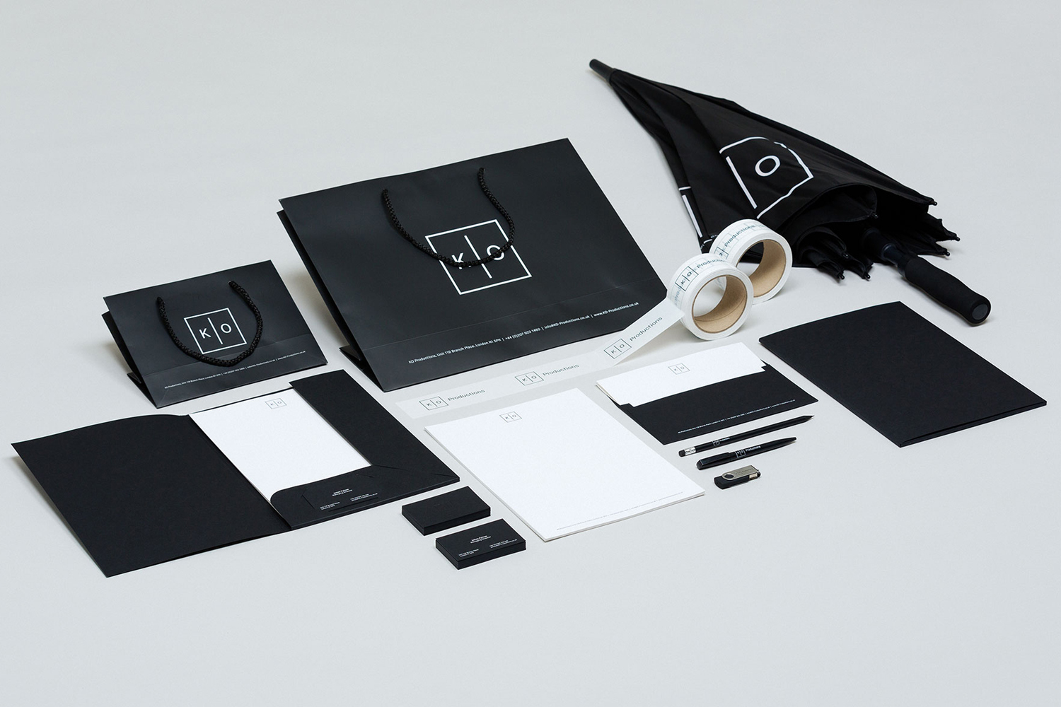 A flat lay of KO Productions brand identity items, including black paper bags, stationery, pens, and an umbrella on a white background.