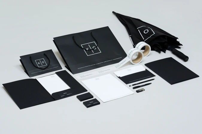 A flat lay of KO Productions brand identity items, including black paper bags, stationery, pens, and an umbrella on a white background.