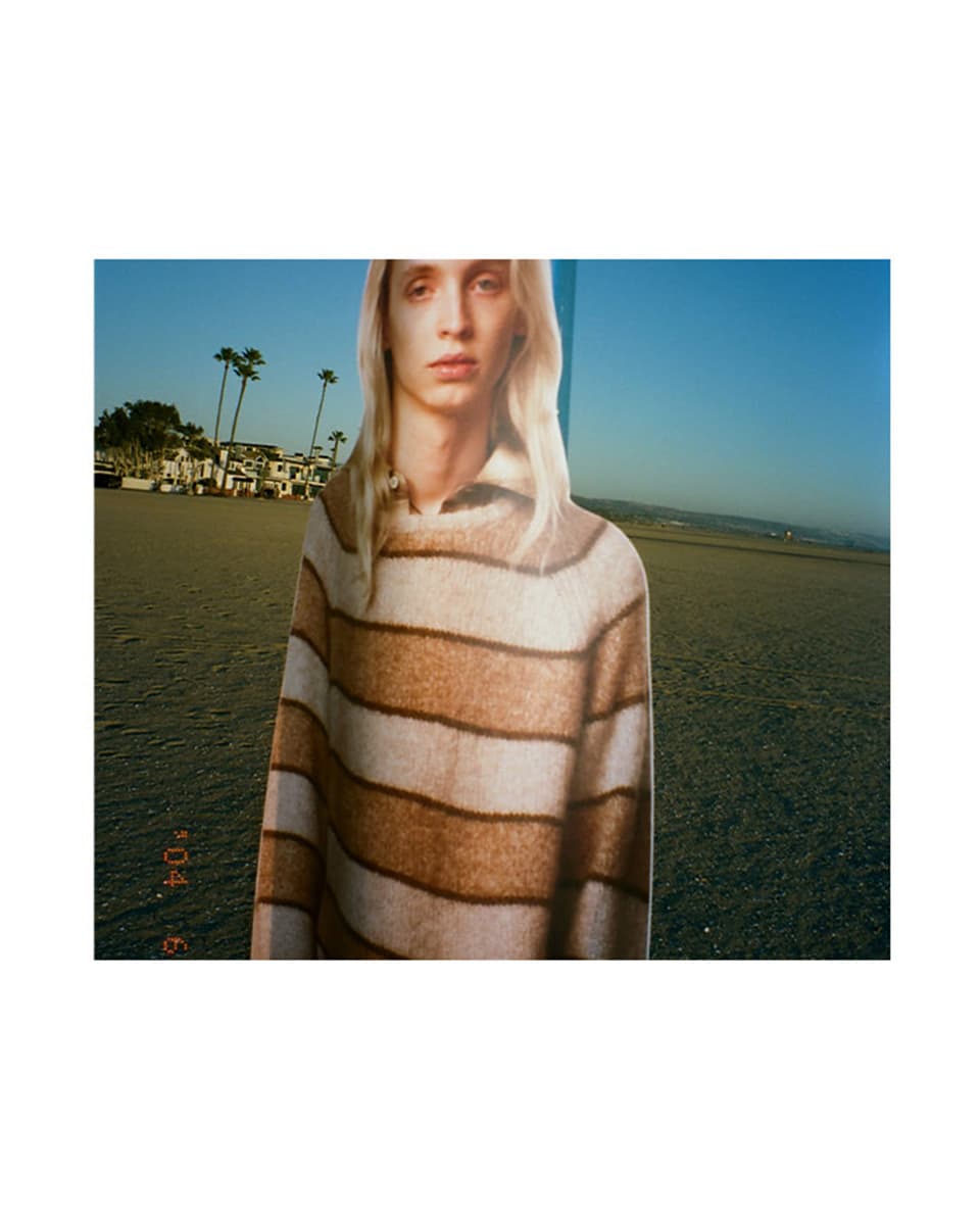 Cut-out figure of a person with long blonde hair wearing a striped sweater outdoors against a coastal landscape background.