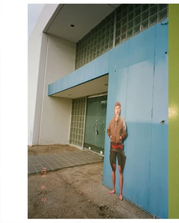 Full-length cut-out figure of a person pasted against a blue building exterior wall with glass block windows.