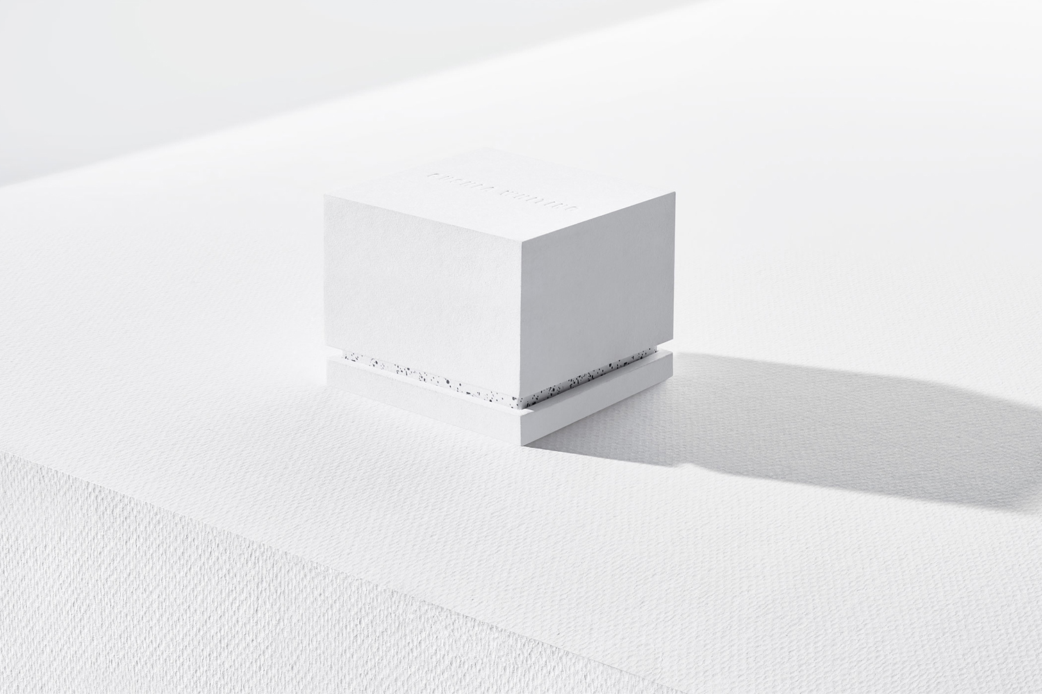 White textured cubic ring box featuring subtle embossed branding on a bright white seamless studio background.