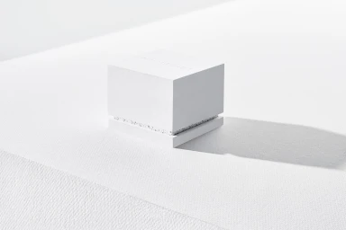 White textured cubic ring box featuring subtle embossed branding on a bright white seamless studio background.