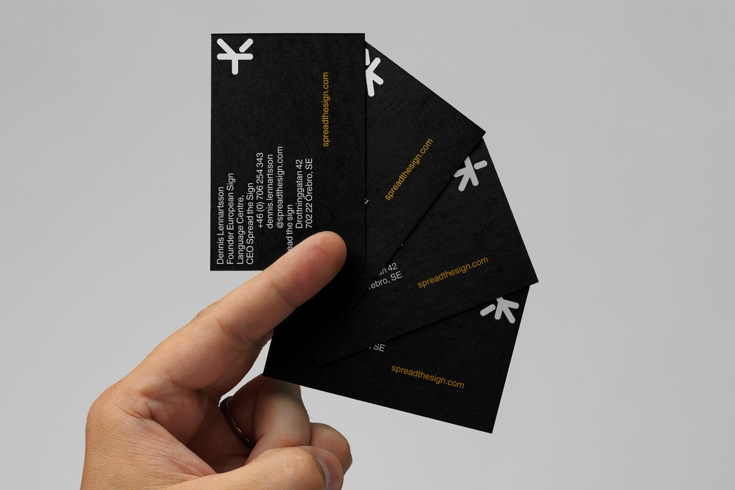 A hand holding a stack of four black business cards with white typography against a plain light grey background.
