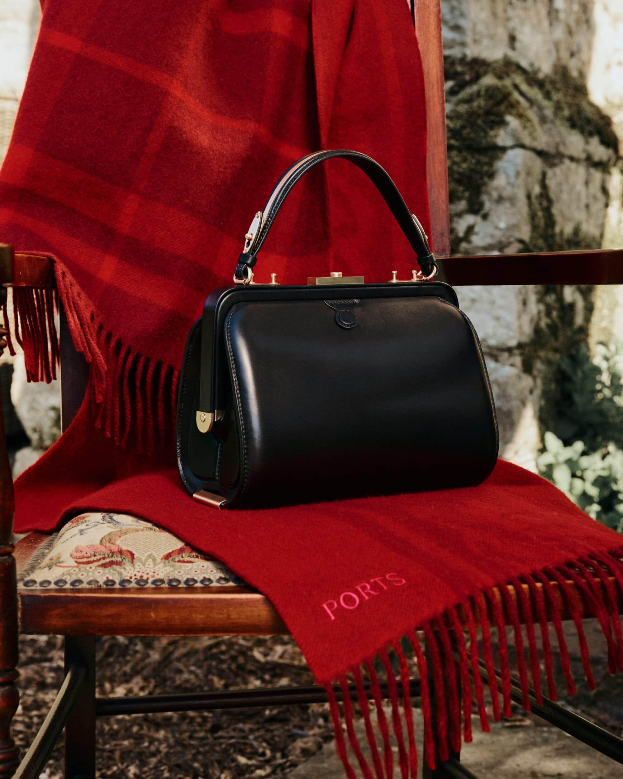 Black leather handbag resting on a red fringed blanket draped over a wooden chair outdoors.