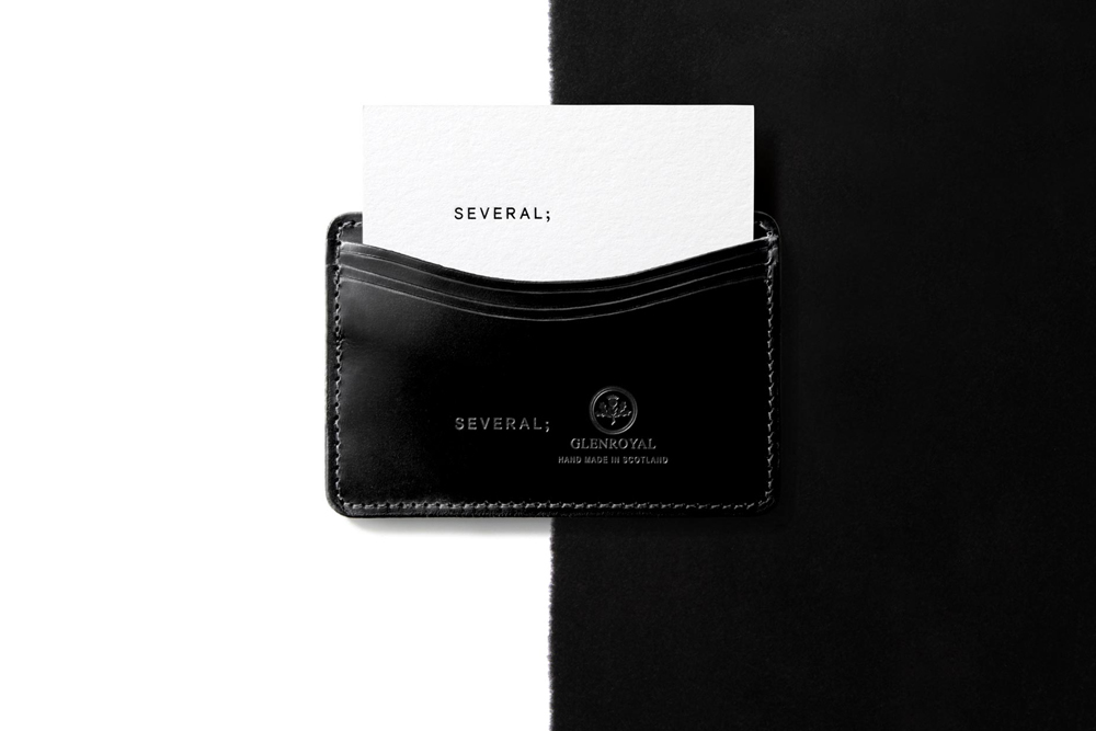 Black leather cardholder holding a white business card with branded text against a split black and white background.