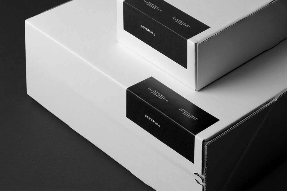 Two white packaging boxes with black branded label wraps on a dark surface
