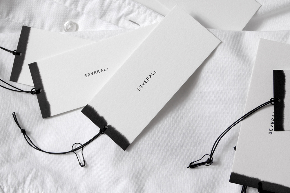 Several brand clothing tags with black dip-dyed ends and strings resting on a white collared shirt