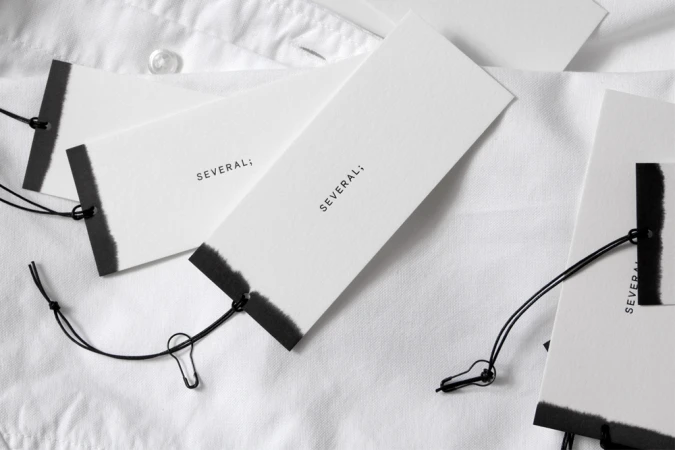 Several brand clothing tags with black dip-dyed ends and strings resting on a white collared shirt