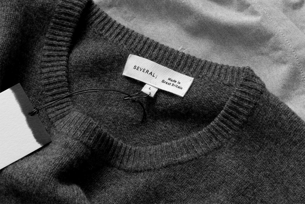 Close-up monochrome view of a Several brand knit sweater collar with woven label and hang tag against a textured fabric background