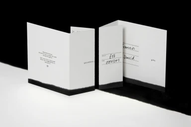 Folded paper cards with printed text and handwritten details set against a contrasting black and white background.