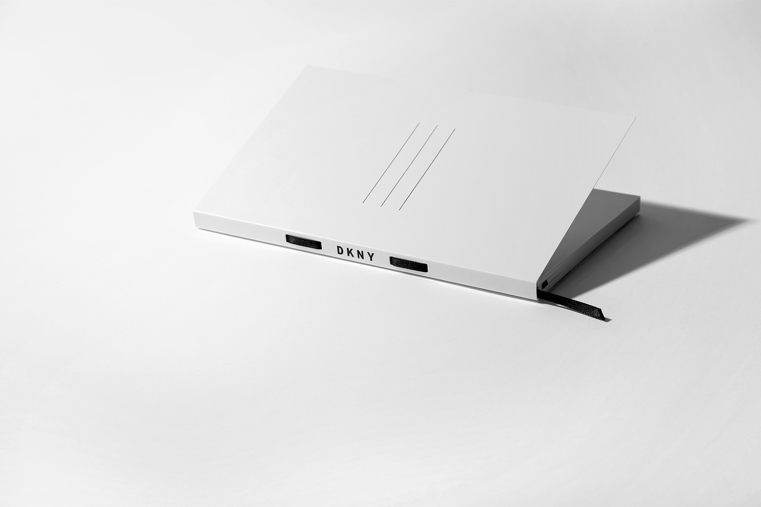 White DKNY branded notebook resting on a clean white surface with sharp shadows cast beside it.