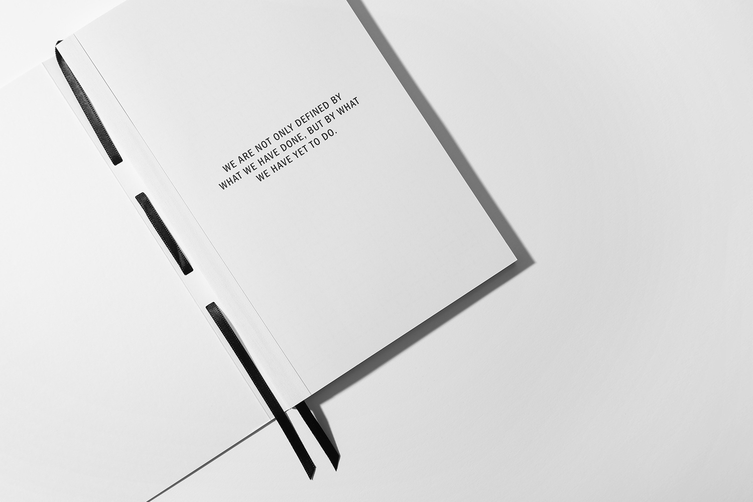 Open white notebook with black ribbon bookmarks and bold typography on a seamless light background.