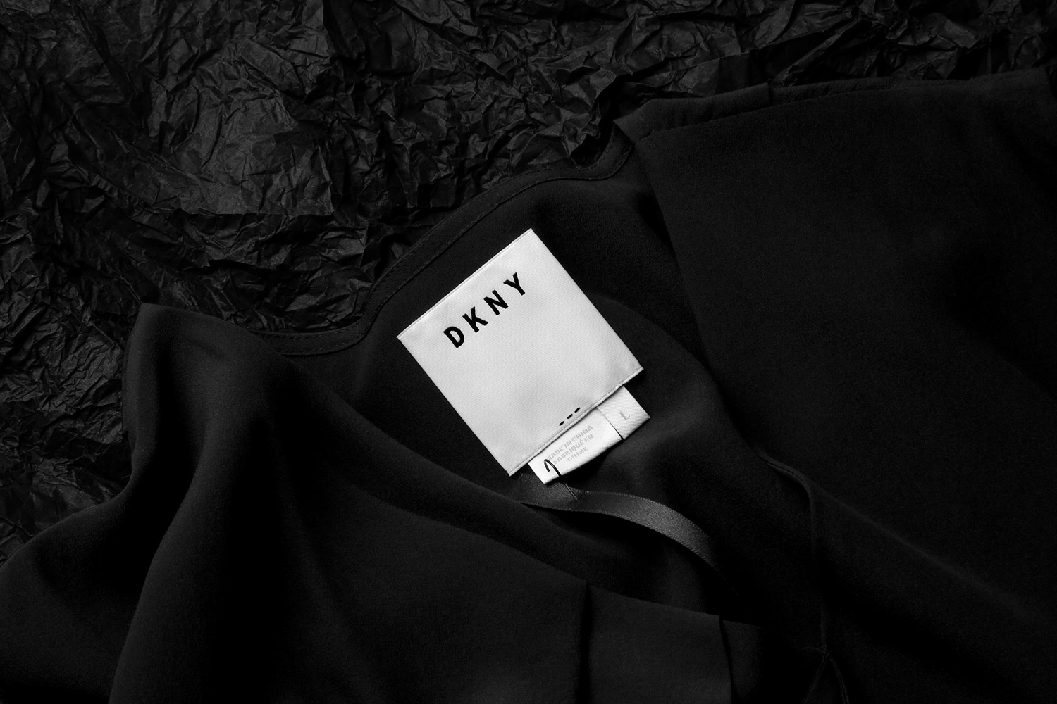 Close-up of a white clothing label with DKNY logo stitched onto black fabric against a textured black background