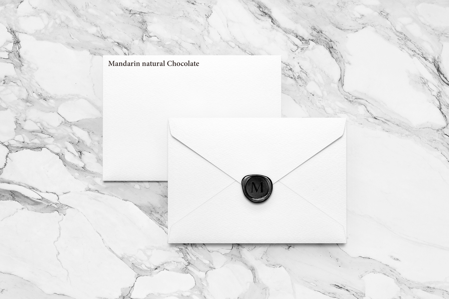Two white envelopes on a grey marble background, one sealed with a black wax stamp bearing the letter M.