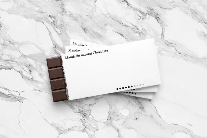 Stacked white chocolate packaging for Mandarin natural Chocolate resting on a white marble surface