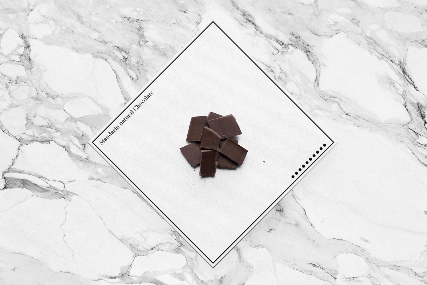 Dark chocolate pieces arranged on a square white card over a white marble surface for Mandarin natural Chocolate brand identity