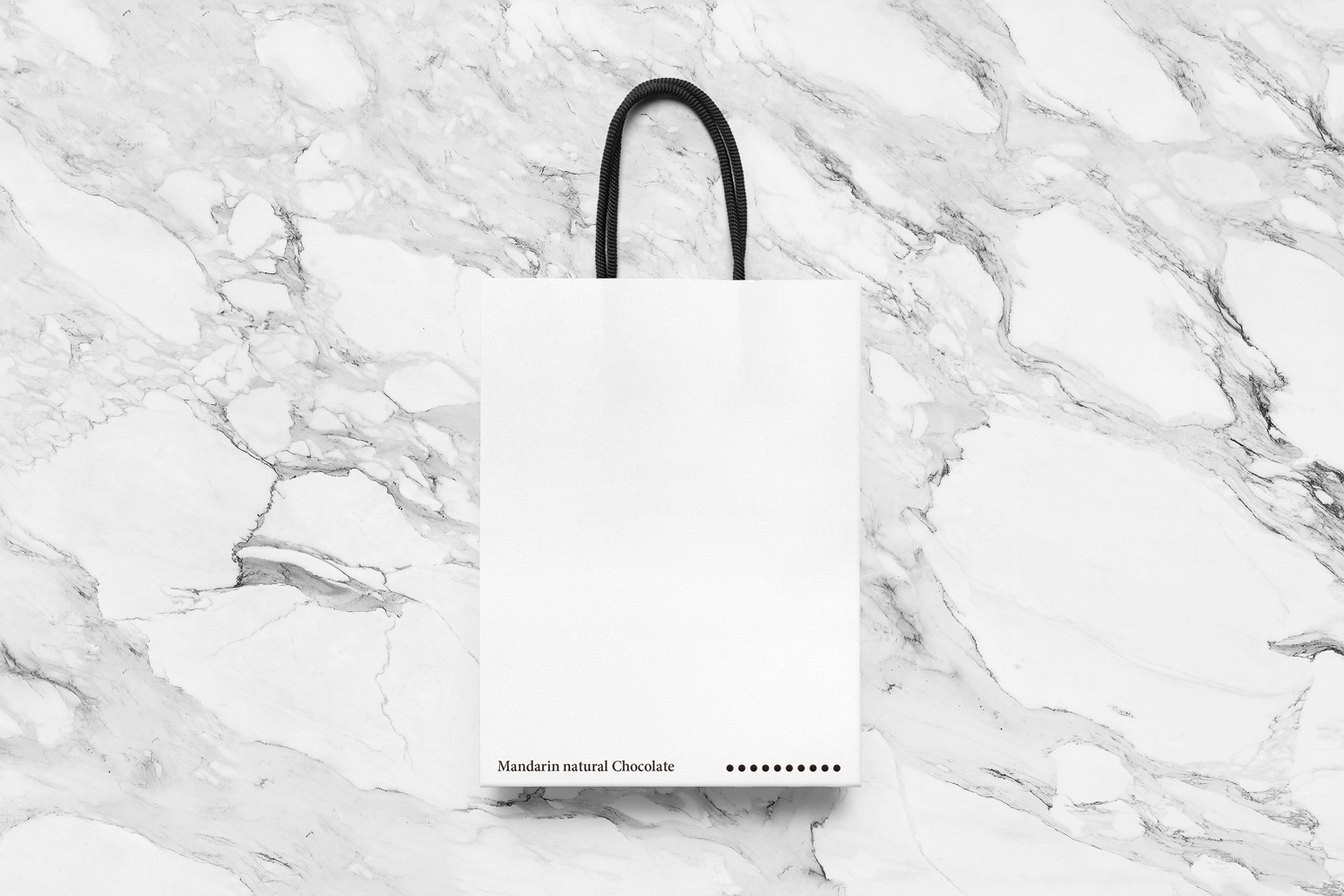 White paper shopping bag with black rope handles resting on a white marble surface.