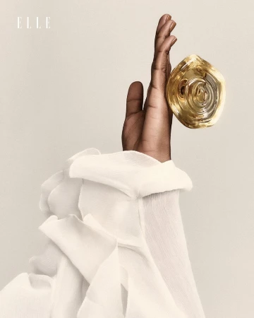Elegant hand with bold gold ring, showcasing a textured white ruffled sleeve against a neutral backdrop. High-fashion jewelry detail.