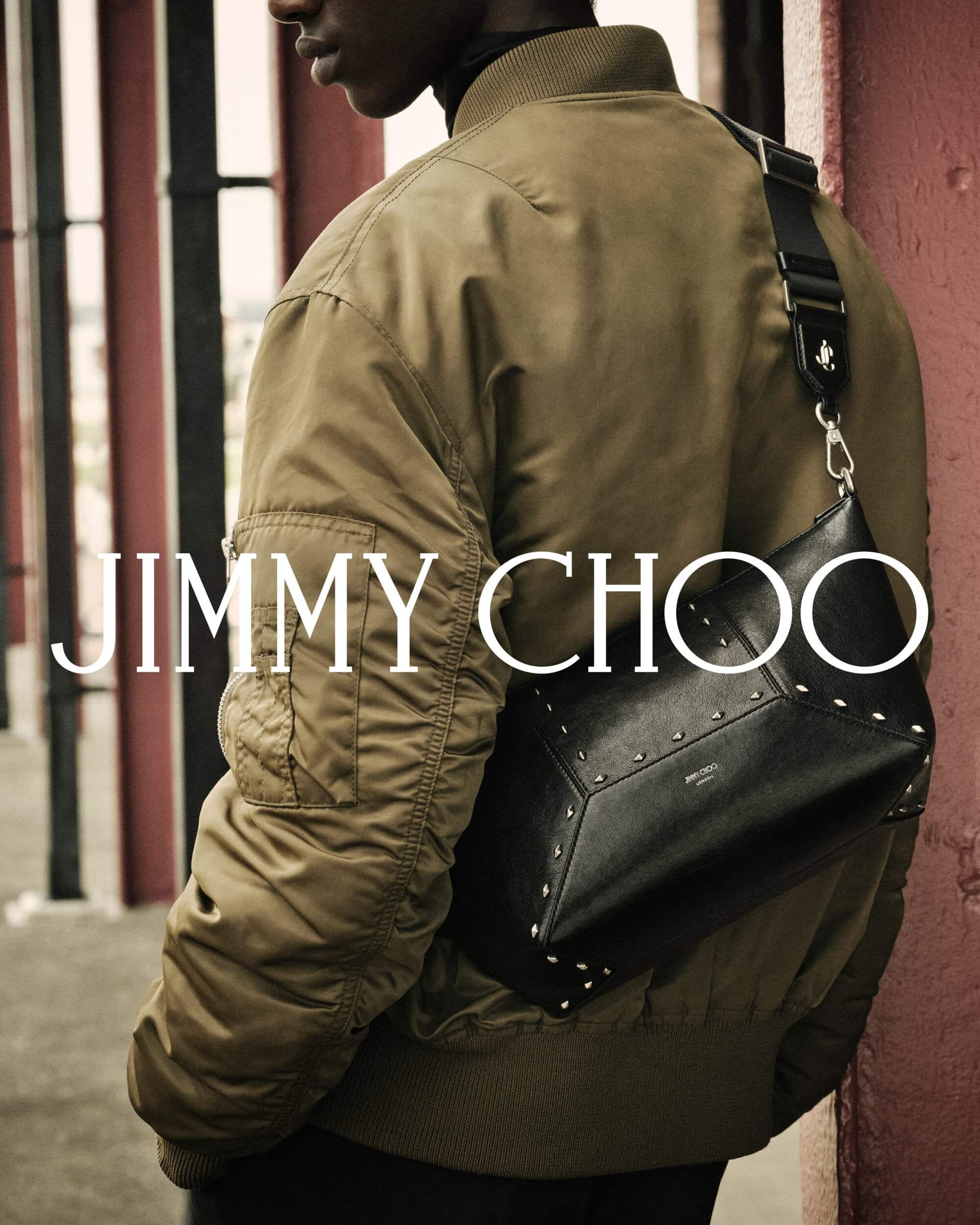 Close-up of a model wearing an olive green bomber jacket and carrying a black studded leather crossbody bag by Jimmy Choo.