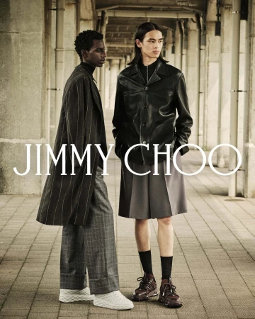Two male models posing under a stone arcade wearing dark coats and patterned trousers for Jimmy Choo Fall 2025 campaign.