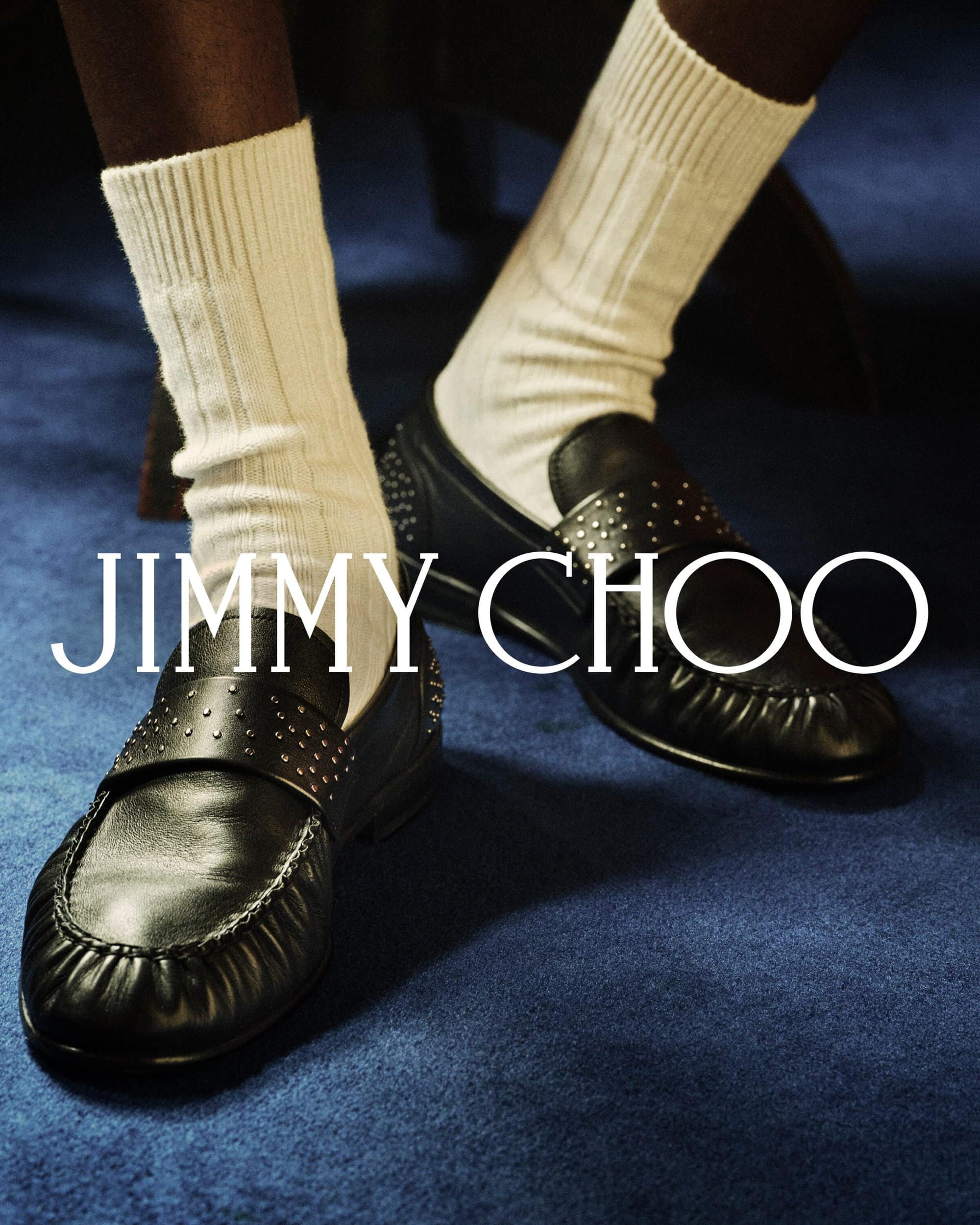Close-up of black studded leather loafers and white ribbed socks against a deep blue carpet