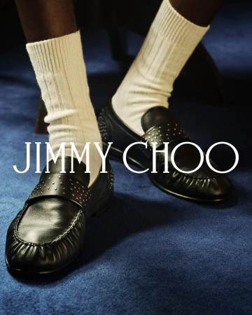 Close-up of black studded leather loafers and white ribbed socks against a deep blue carpet