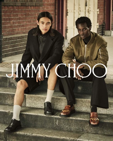 Two male models seated on stone steps outdoors wearing outerwear and leather shoes for Jimmy Choo