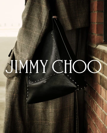 Close-up of a person wearing a plaid coat carrying a large black studded handbag beside a brick wall